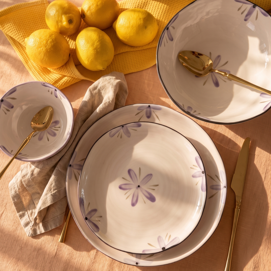 Purple Dinnerware set with floral patterns on a table with lemons and a vase.