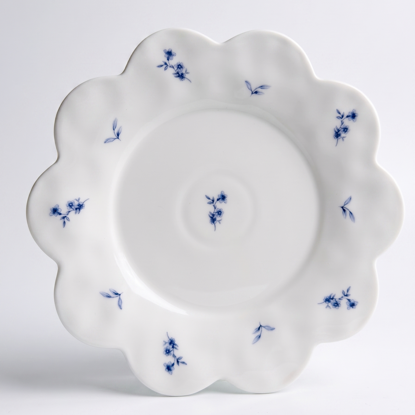 white scalloped dessert plate with small blue flower pattern on white background