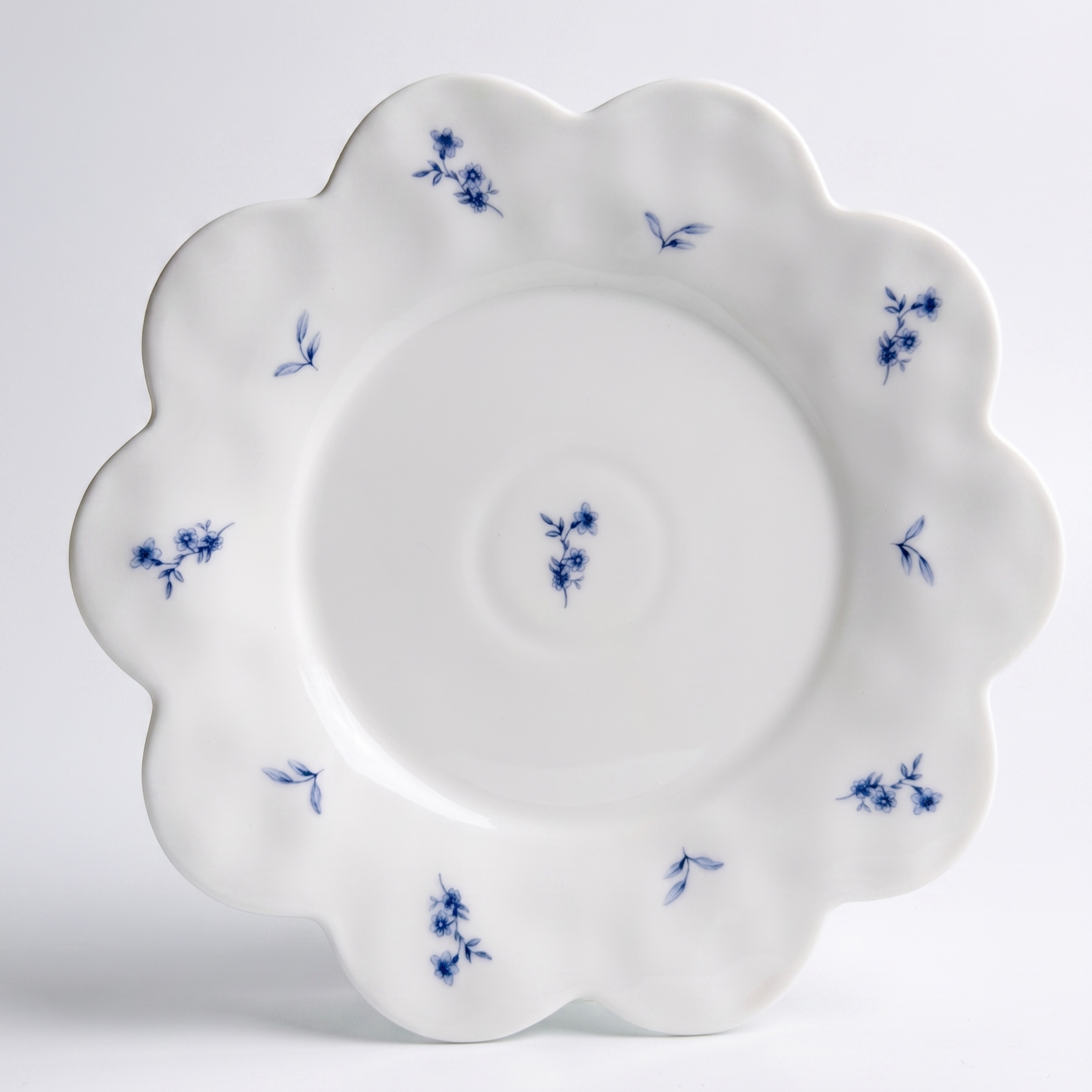 white scalloped dessert plate with small blue flower pattern on white background