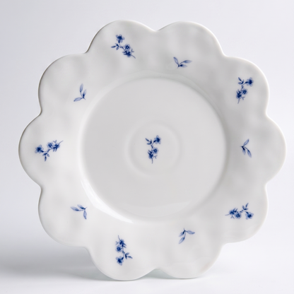white scalloped dessert plate with small blue flower pattern on white background