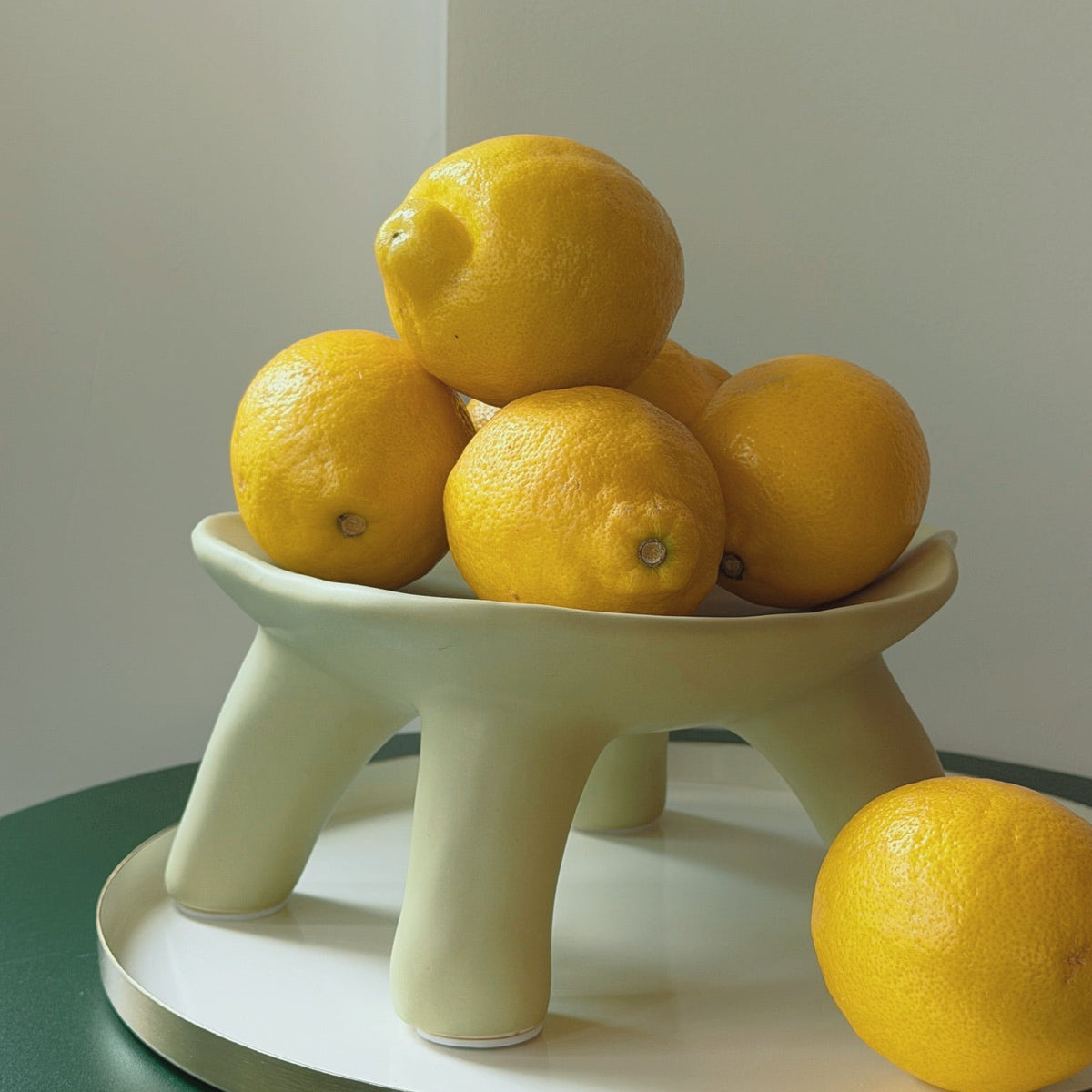 Cream Pedestal Bowl Vase on splayed legs holding a stacked pile of lemons on a green side table.