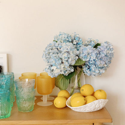 Frosted amber and blue Sea Glass cups on a wood cabinet styled with blue hydrangeas and lemons.