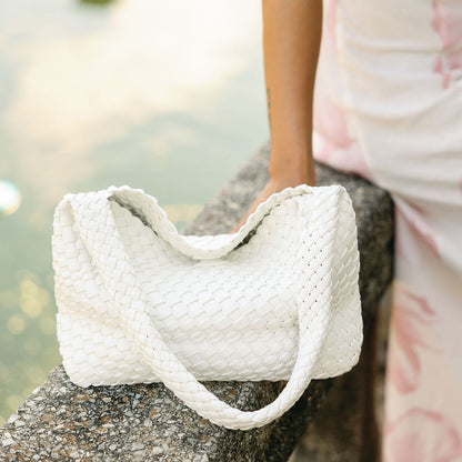White textured handbag on a stone surface with a blurred natural background