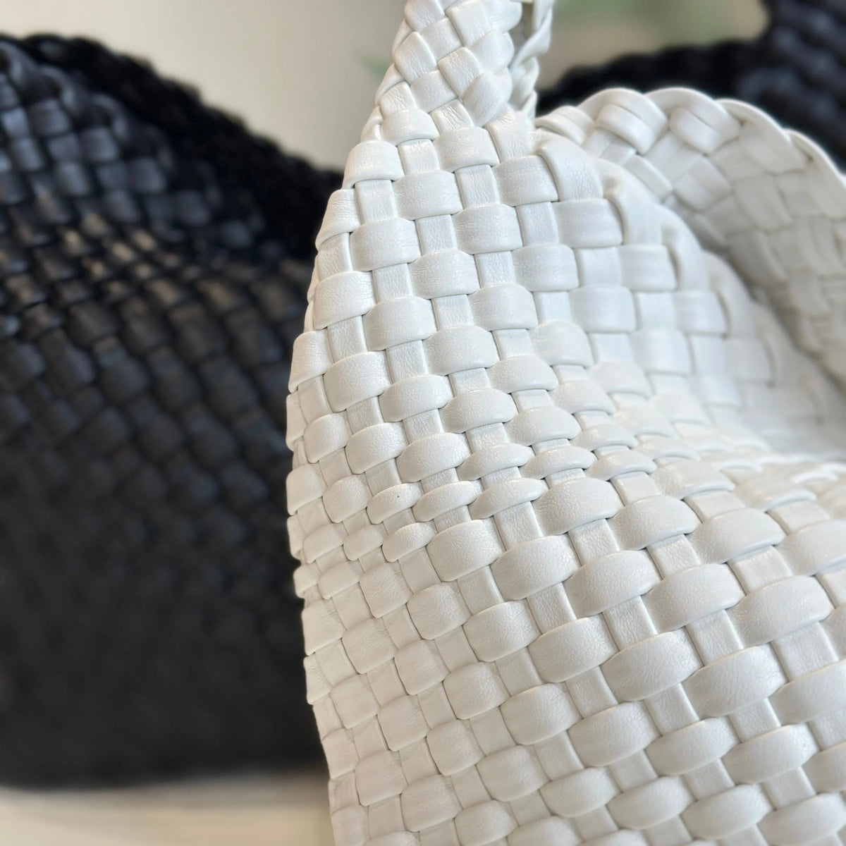 Close-up of white woven leather tote's basketweave texture, with a black woven bag behind