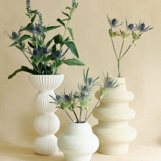 White ribbed Pleated Column Vase grouped with textured vases holding blue thistle and veronica on linen.