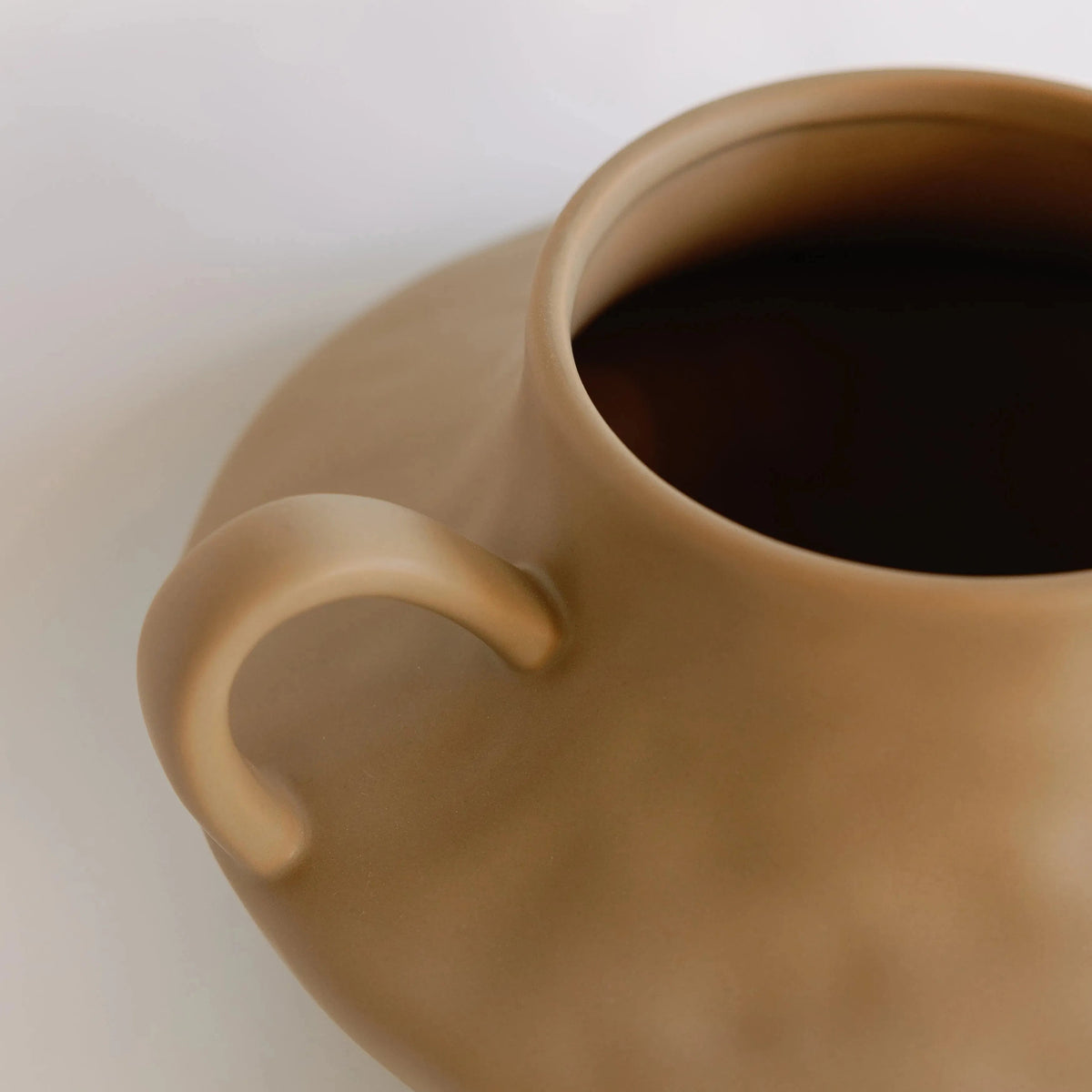 Close-up of tan amphora ceramic vase rim and one curved loop handle, matte finish detail