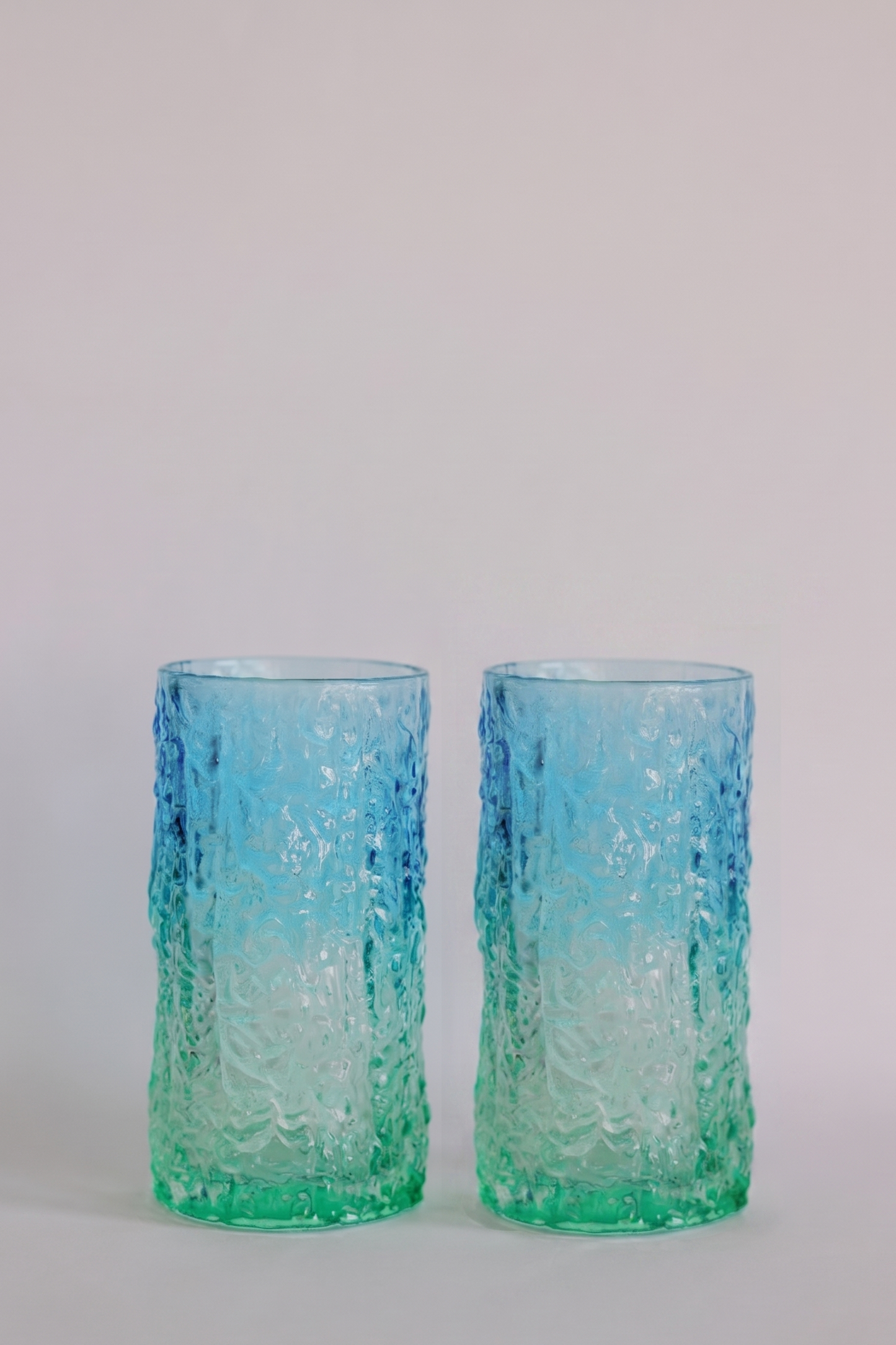 Two textured glass tumblers with a blue-to-green gradient, standing side by side against a light gray background.