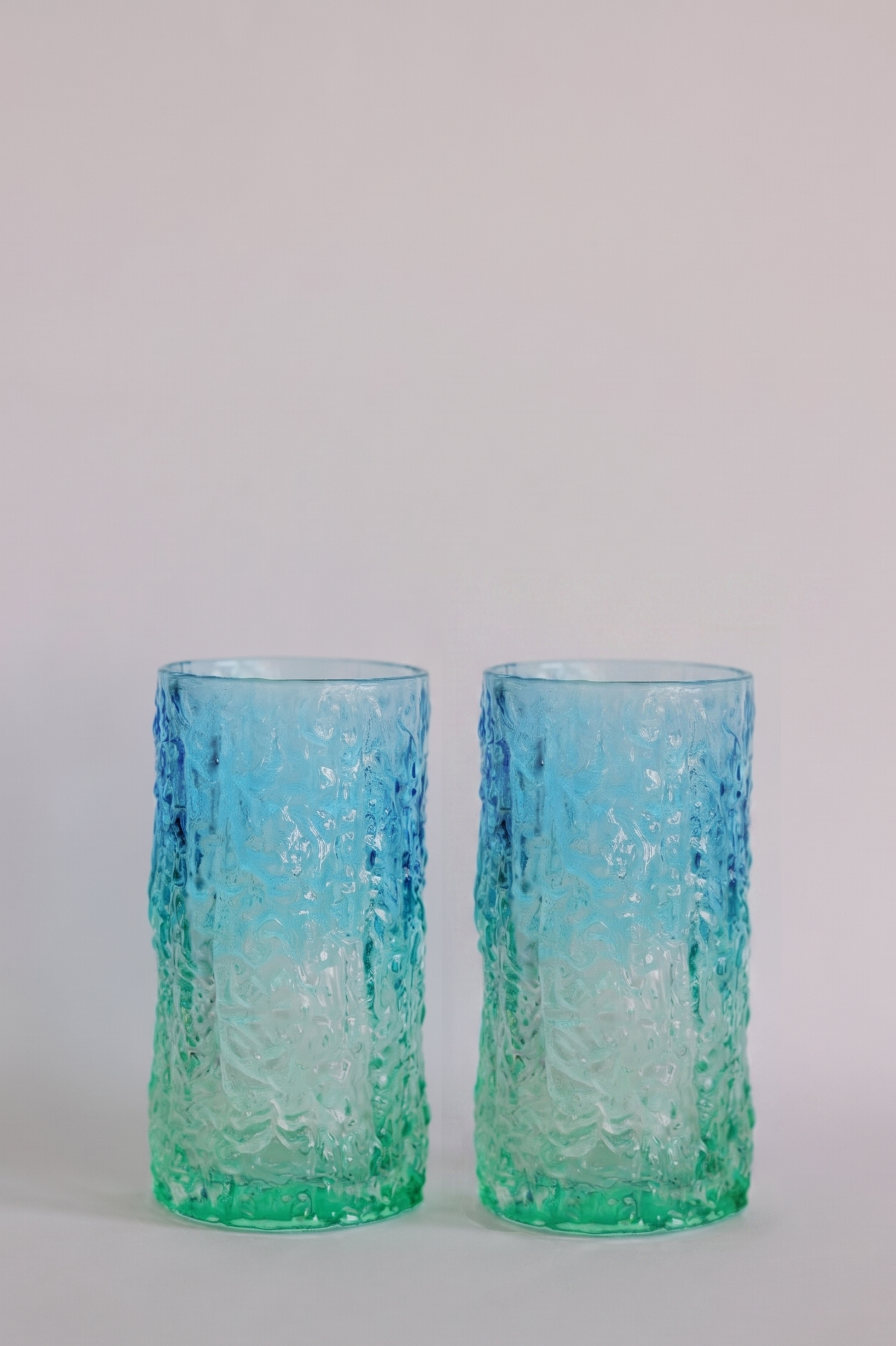 Two textured glass tumblers with a blue-to-green gradient, standing side by side against a light gray background.