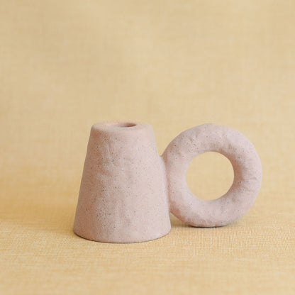 Two pink textured ceramic candle holders, a cone and a ring shape, on a yellow backdrop.