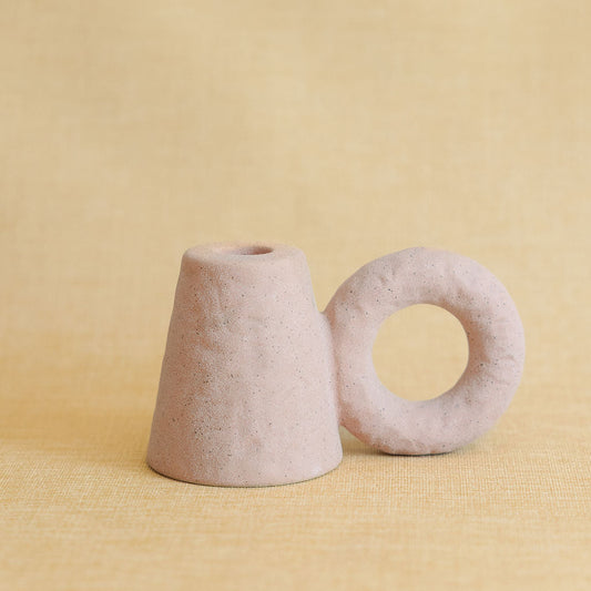 Two pink textured ceramic candle holders, a cone and a ring shape, on a yellow backdrop.