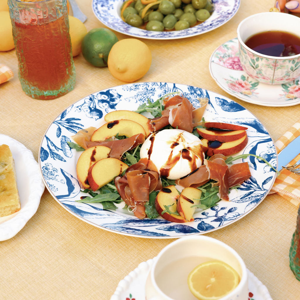 Blue and white floral porcelain plate with peach burrata salad, styled on a yellow outdoor table.