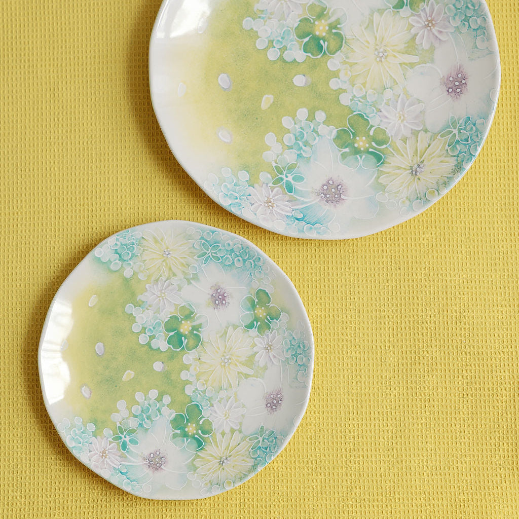Two Watercolor Meadow porcelain plates with green, white and aqua floral print on a yellow textile.