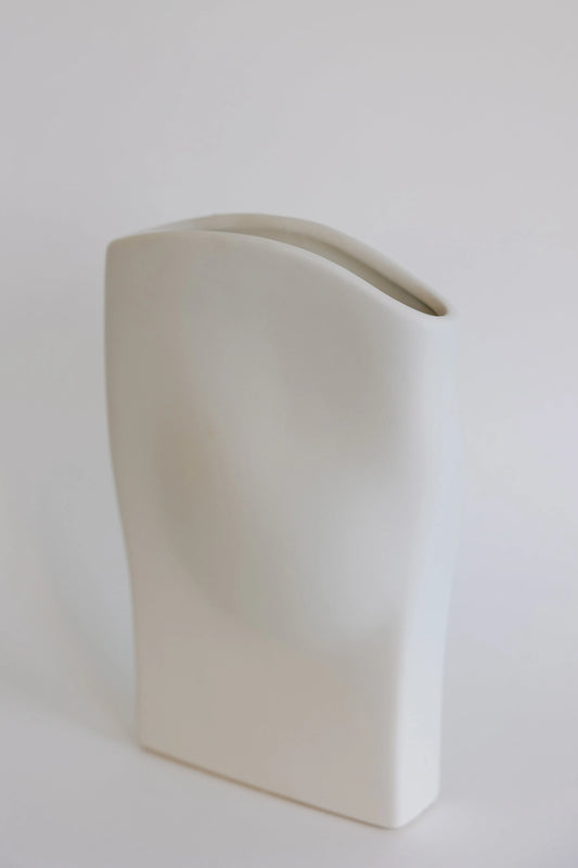 Wave ceramic vase in cream shown at an angle, flat draped body with sloping rim opening